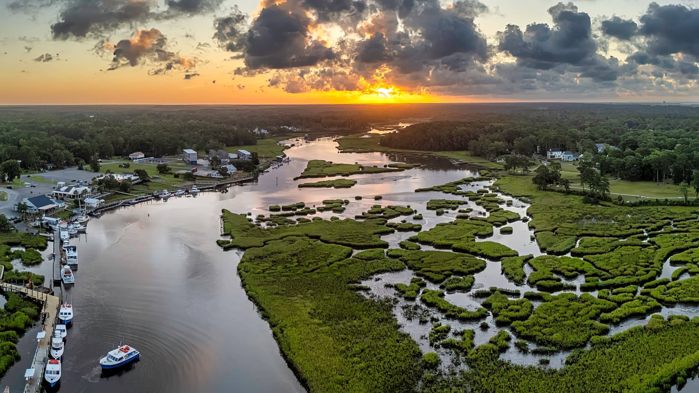 Boats on calm Little River waters at sunset over the marsh