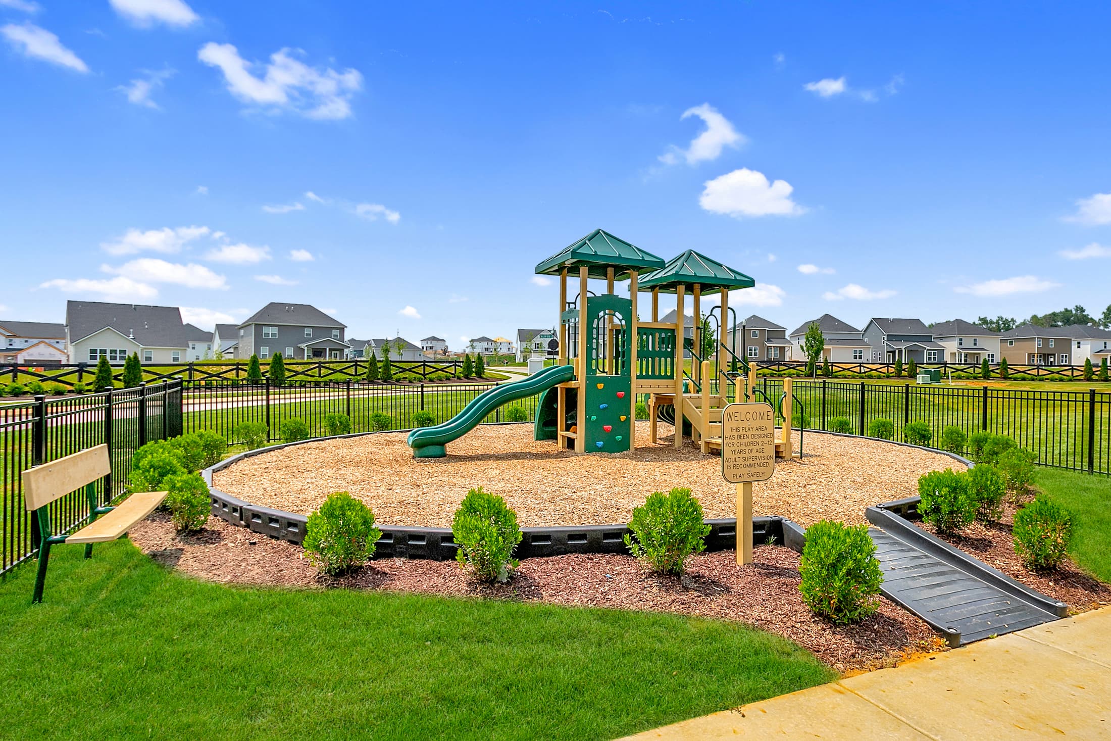green playground with landscaping and a bench